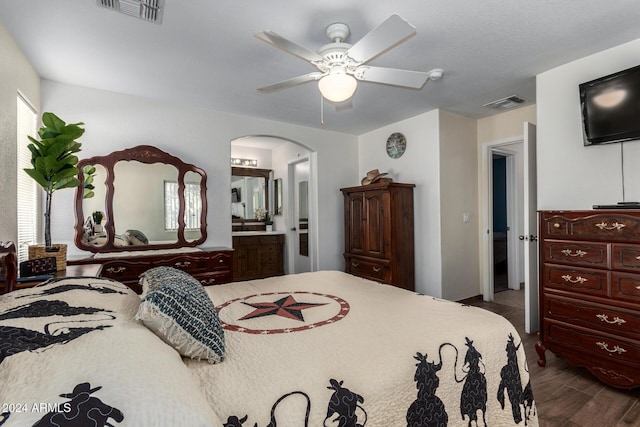 bedroom featuring arched walkways, ceiling fan, wood finished floors, visible vents, and ensuite bath