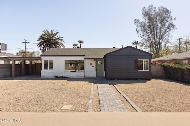 view of front facade with a carport, board and batten siding, concrete driveway, and fence