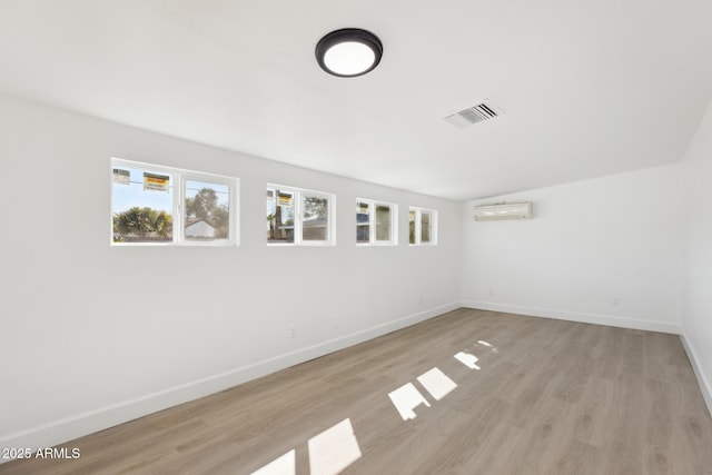 spare room featuring an AC wall unit, light wood-style flooring, baseboards, and visible vents