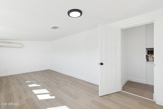 spare room with a wall unit AC, light wood-style flooring, and baseboards