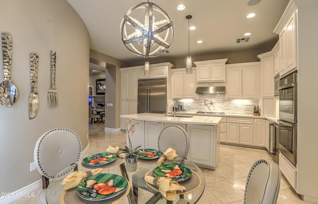 kitchen with hanging light fixtures, light tile patterned floors, appliances with stainless steel finishes, a kitchen island with sink, and white cabinets