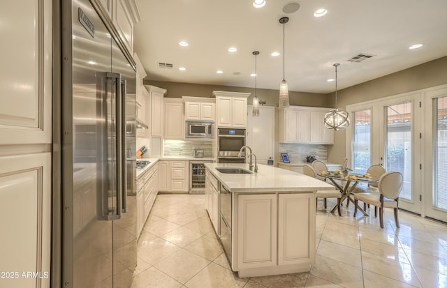 kitchen with sink, built in appliances, pendant lighting, beverage cooler, and a kitchen island with sink