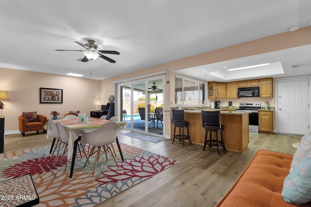 dining room with light wood-type flooring, a tray ceiling, ceiling fan, a skylight, and baseboards
