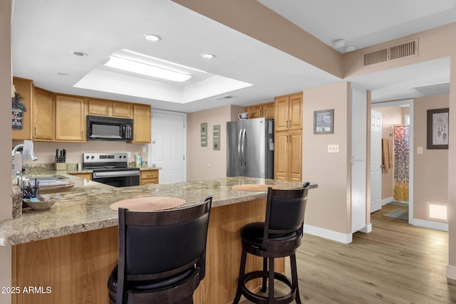 kitchen featuring appliances with stainless steel finishes, a sink, a raised ceiling, baseboards, and a peninsula