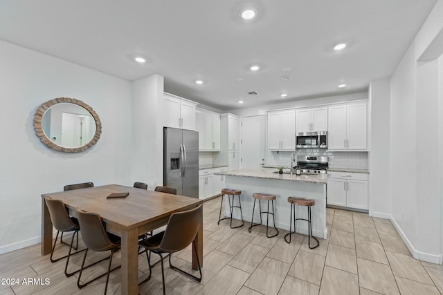 kitchen featuring light stone counters, white cabinetry, stainless steel appliances, and an island with sink