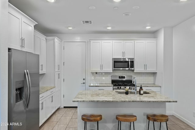 kitchen featuring a kitchen island with sink, white cabinets, a kitchen breakfast bar, decorative backsplash, and appliances with stainless steel finishes