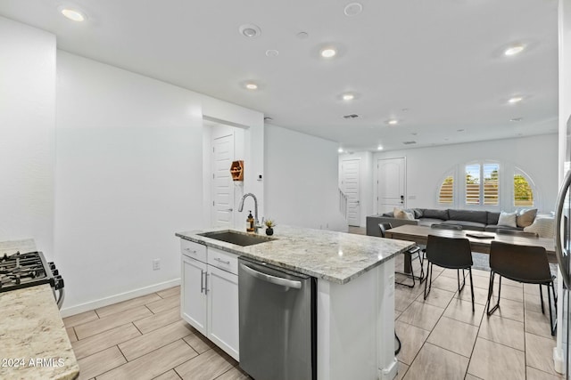 kitchen with sink, stainless steel appliances, light stone counters, a center island with sink, and white cabinets