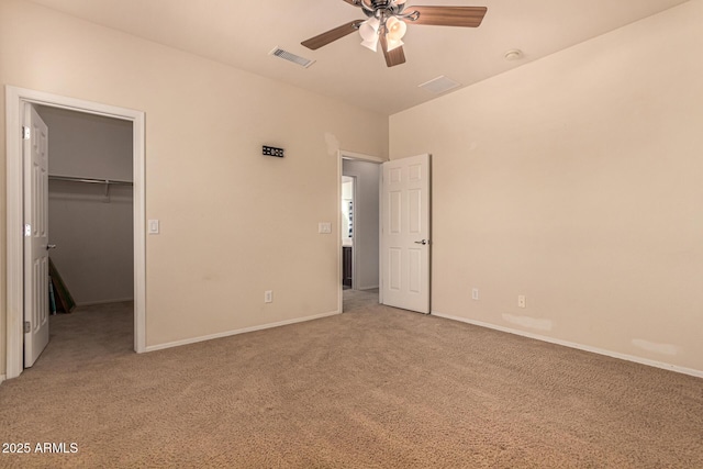 unfurnished bedroom featuring a walk in closet, light carpet, ceiling fan, and a closet