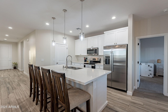 kitchen with white cabinetry, appliances with stainless steel finishes, a kitchen island with sink, hanging light fixtures, and sink