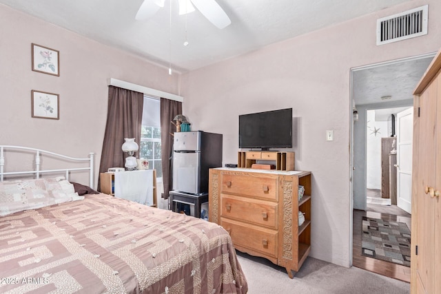 bedroom featuring stainless steel fridge, light colored carpet, and ceiling fan