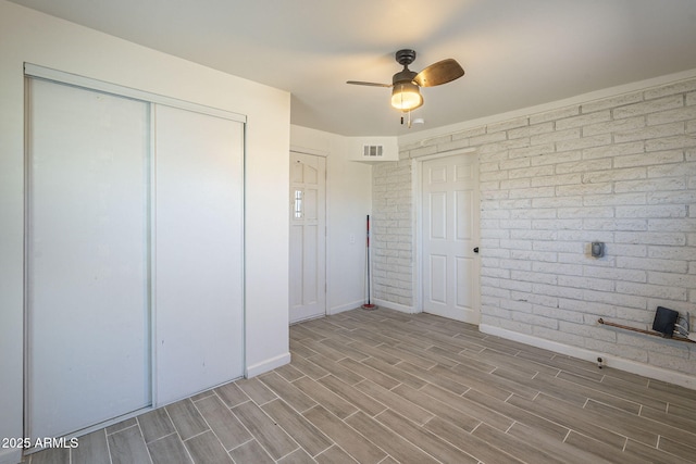 unfurnished bedroom with brick wall, ceiling fan, and a closet