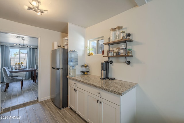 kitchen featuring light stone counters, white cabinets, and stainless steel refrigerator