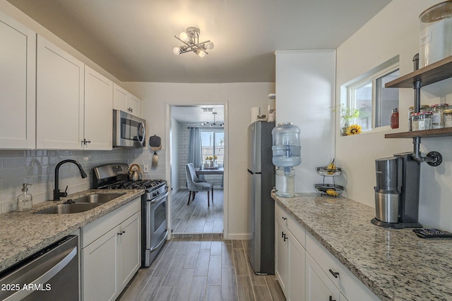 kitchen with sink, white cabinets, backsplash, light stone counters, and stainless steel appliances