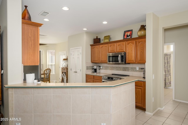 kitchen with light tile patterned floors, recessed lighting, stainless steel appliances, a peninsula, and light countertops