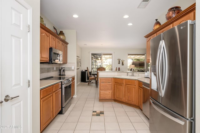 kitchen featuring visible vents, brown cabinetry, appliances with stainless steel finishes, light countertops, and a sink