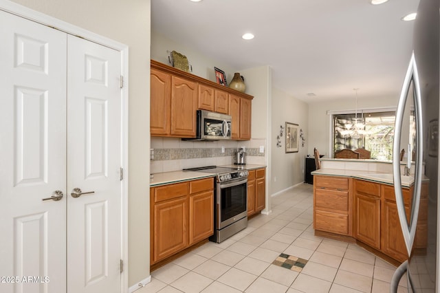 kitchen with light tile patterned floors, stainless steel appliances, light countertops, hanging light fixtures, and brown cabinetry