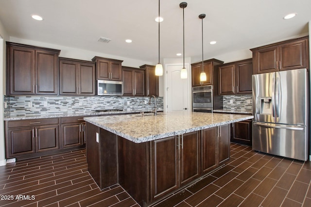 kitchen with stainless steel appliances, pendant lighting, dark brown cabinets, and an island with sink