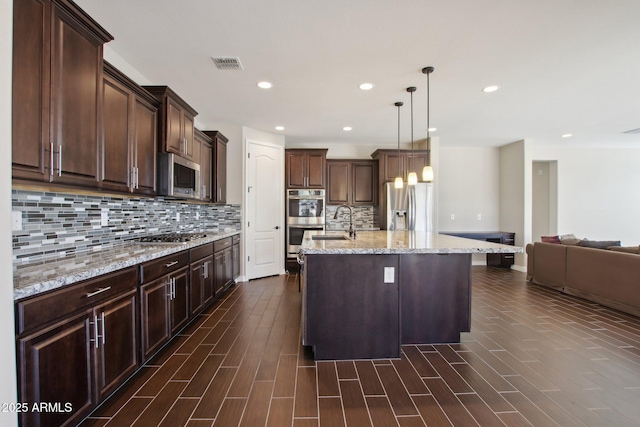 kitchen with backsplash, a kitchen island with sink, pendant lighting, and appliances with stainless steel finishes