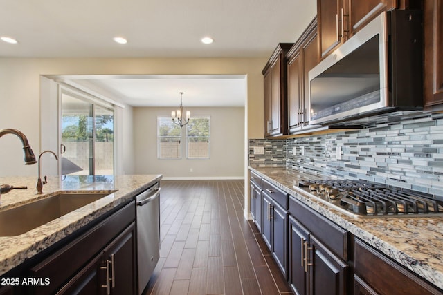 kitchen featuring sink, light stone countertops, dark brown cabinetry, a chandelier, and appliances with stainless steel finishes