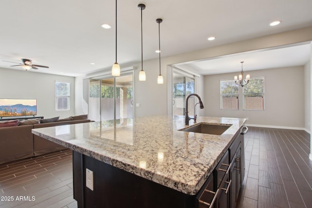 kitchen with sink, hanging light fixtures, an island with sink, and light stone counters