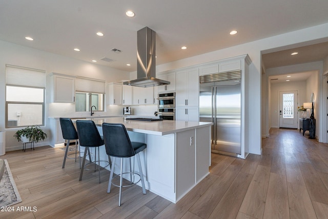 kitchen with a center island, white cabinets, light hardwood / wood-style flooring, island range hood, and appliances with stainless steel finishes