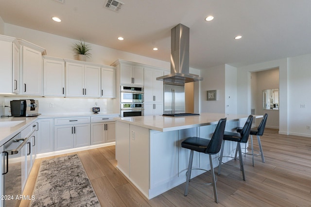 kitchen featuring appliances with stainless steel finishes, island range hood, white cabinetry, and light wood-type flooring