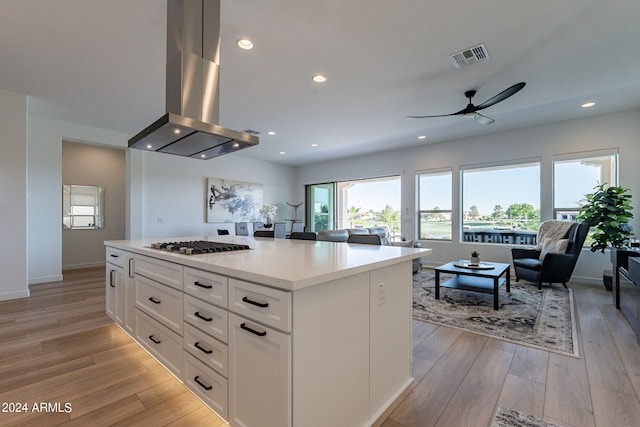 kitchen with ceiling fan, light hardwood / wood-style flooring, a kitchen island, white cabinets, and island exhaust hood