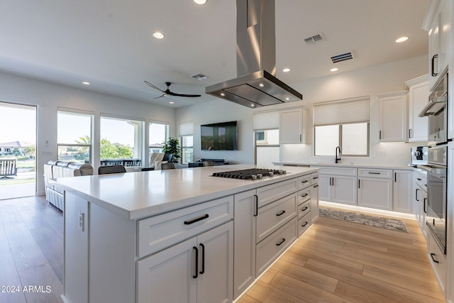 kitchen with white cabinets, light hardwood / wood-style flooring, island exhaust hood, ceiling fan, and a kitchen island