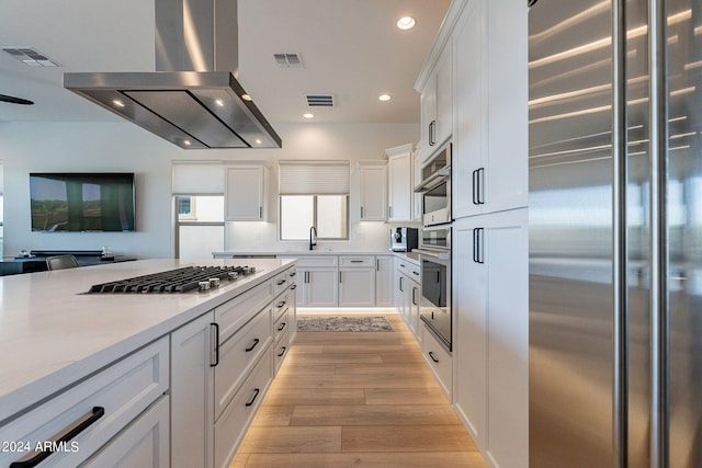 kitchen with white cabinets, sink, light hardwood / wood-style floors, island range hood, and stainless steel appliances