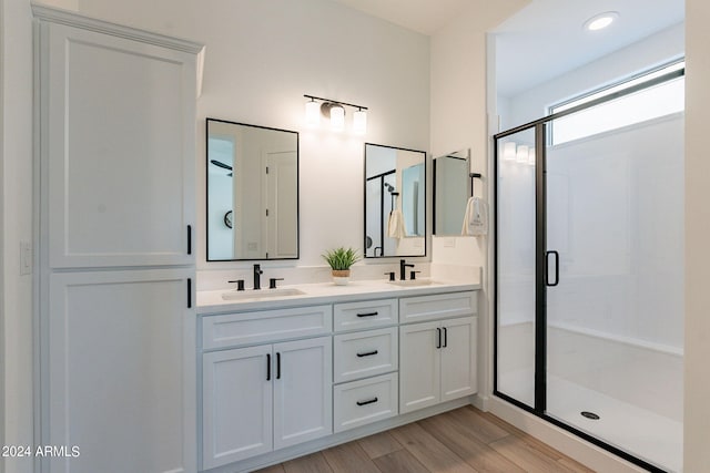 bathroom with a shower with door, oversized vanity, hardwood / wood-style flooring, and double sink