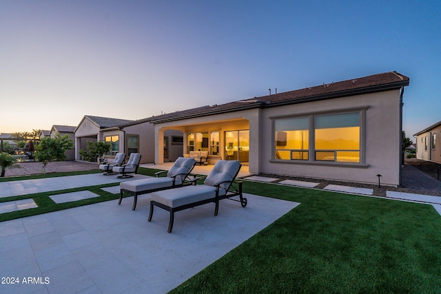 back house at dusk with a garage, an outdoor hangout area, a patio, and a lawn