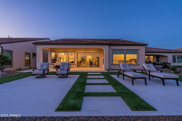 back house at dusk with outdoor lounge area and a patio area