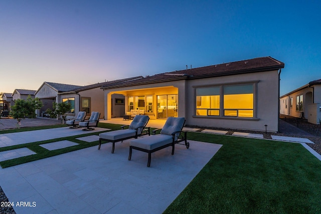 back house at dusk with a yard and a patio