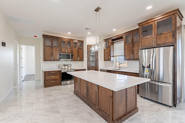 kitchen with decorative light fixtures, a kitchen island, sink, and stainless steel appliances