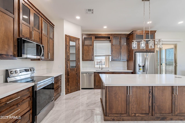 kitchen with stainless steel appliances, a kitchen island, hanging light fixtures, and sink