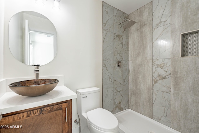 bathroom featuring a tile shower, vanity, and toilet