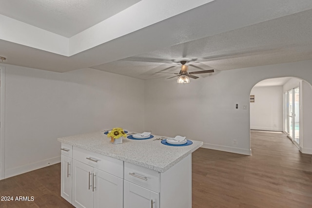 kitchen with ceiling fan, white cabinets, a kitchen island, dark wood-type flooring, and light stone countertops