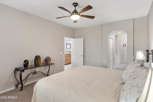 bedroom with arched walkways, light colored carpet, a ceiling fan, baseboards, and ensuite bath