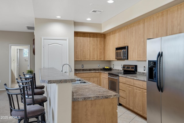 kitchen with stainless steel appliances, visible vents, light brown cabinets, a sink, and a kitchen bar