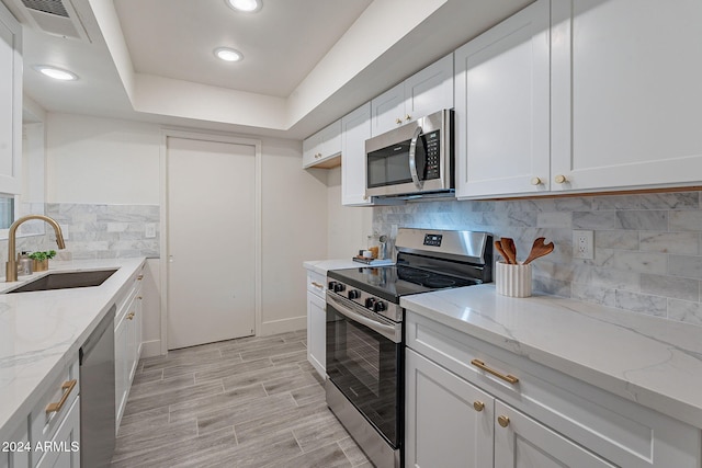 kitchen featuring appliances with stainless steel finishes, light stone counters, white cabinetry, and sink