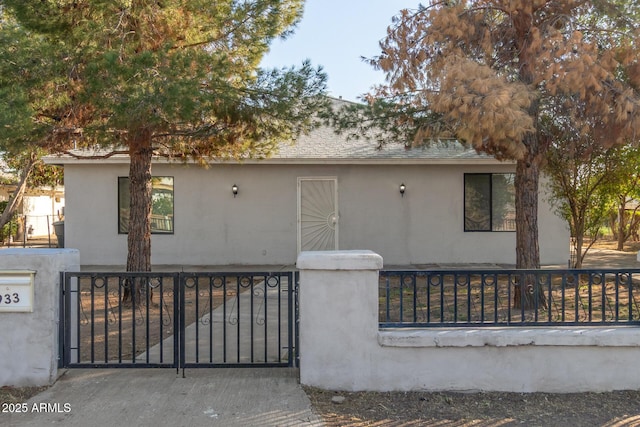 view of front of home featuring roof with shingles, a fenced front yard, a gate, and stucco siding