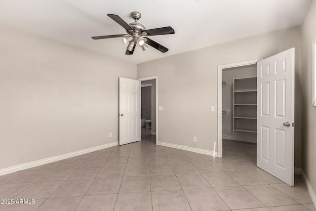 unfurnished bedroom featuring light tile patterned floors, ceiling fan, baseboards, a spacious closet, and a closet