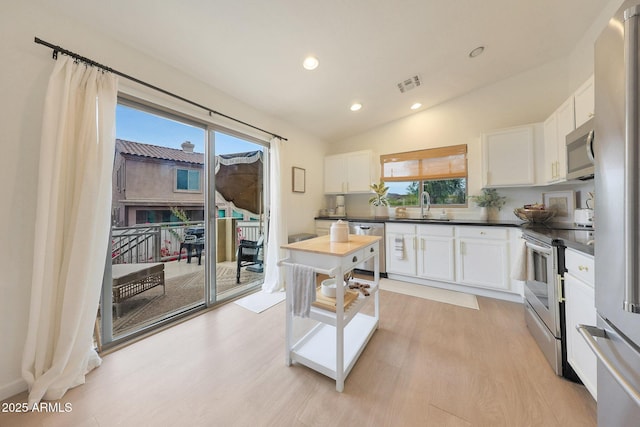 kitchen with sink, appliances with stainless steel finishes, white cabinetry, vaulted ceiling, and light wood-type flooring