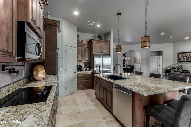 kitchen featuring a kitchen breakfast bar, light stone counters, stainless steel appliances, sink, and pendant lighting