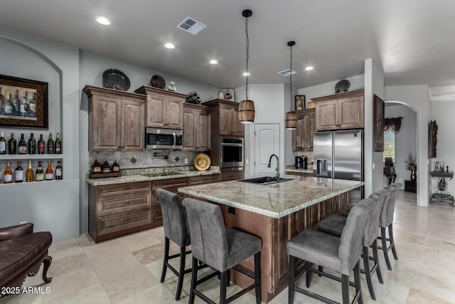 kitchen featuring decorative backsplash, appliances with stainless steel finishes, light stone counters, sink, and an island with sink