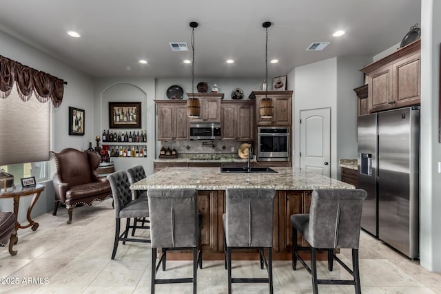 kitchen with appliances with stainless steel finishes, light stone counters, a kitchen island with sink, and sink