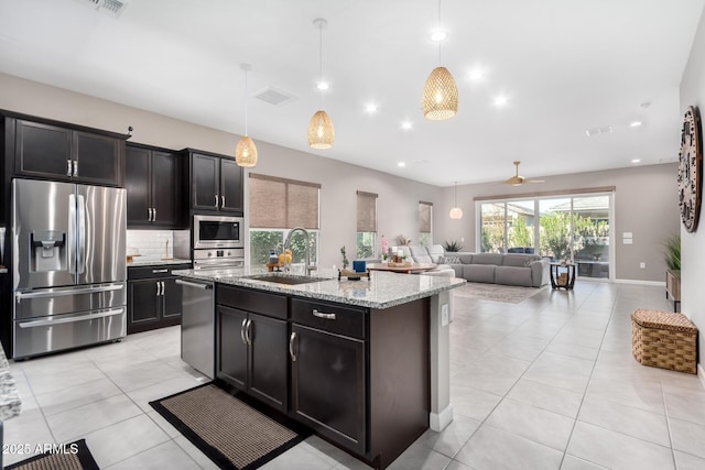 kitchen featuring sink, light stone counters, hanging light fixtures, appliances with stainless steel finishes, and an island with sink