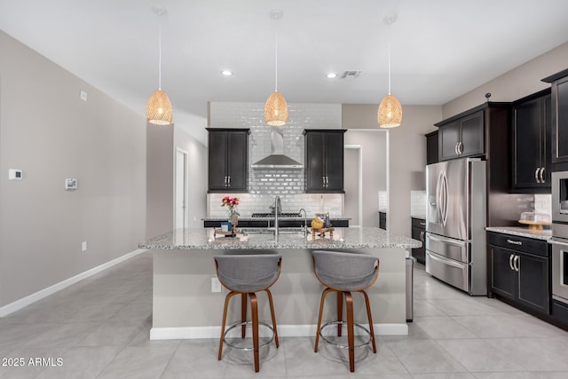 kitchen featuring stainless steel appliances, a kitchen island with sink, and wall chimney exhaust hood