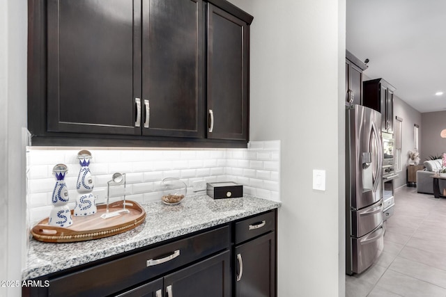 kitchen with tasteful backsplash, light stone countertops, dark brown cabinetry, and stainless steel refrigerator with ice dispenser