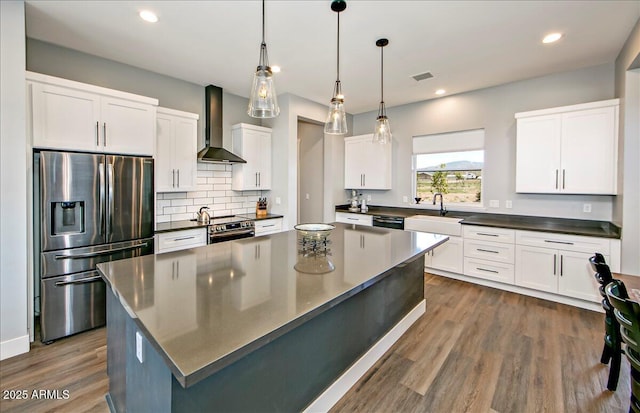 kitchen featuring white cabinetry, stainless steel refrigerator with ice dispenser, wall chimney range hood, a kitchen island, and pendant lighting